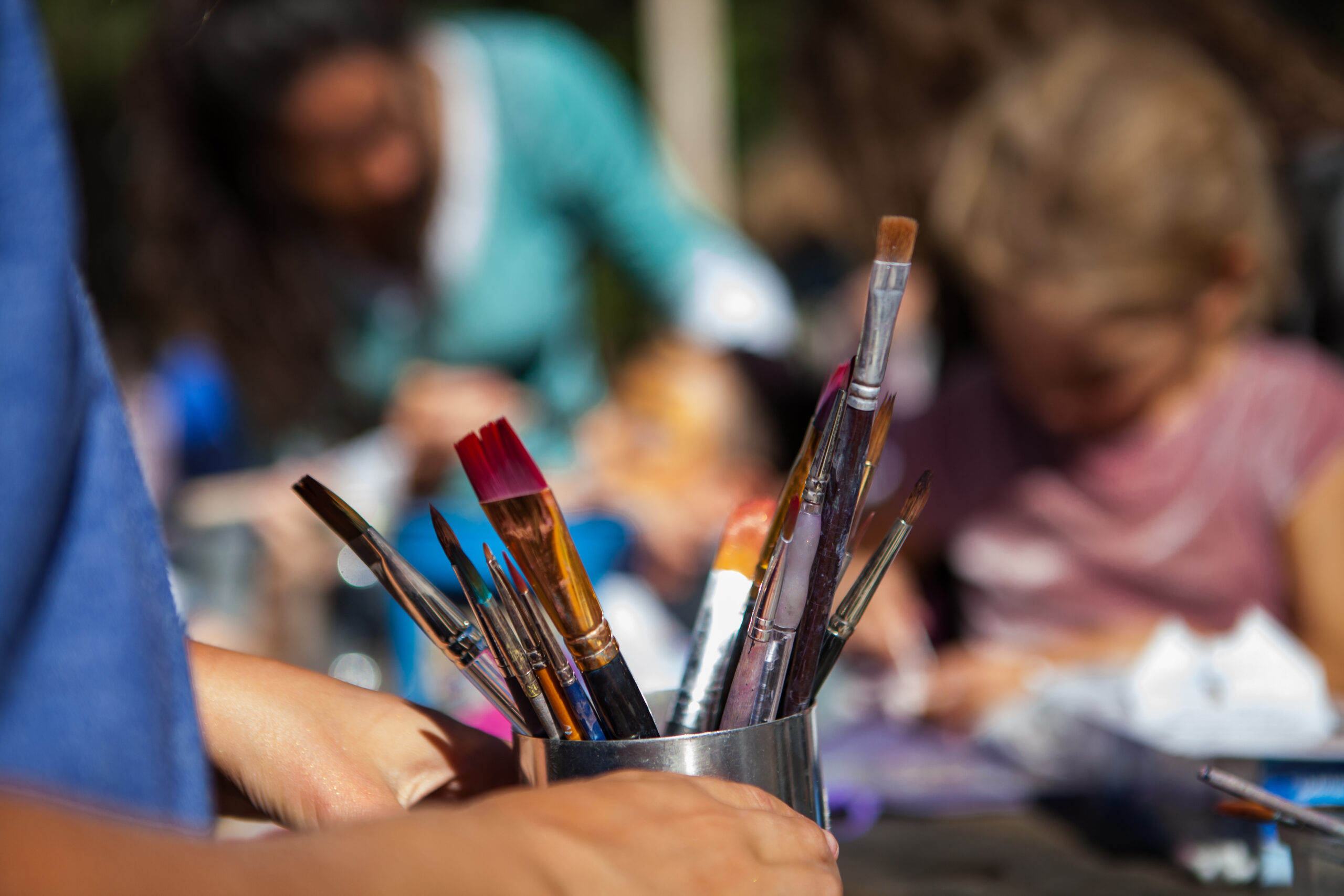 Kid is holding a metal container full of paintbrushes at outdoor arts event